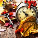 A clock in a pile of colorful fall leaves.