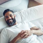 Bearded man smiling while laying on a bed.