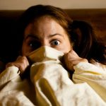 Frightened Woman in Bed with the Sheets Pulled Up to her Face